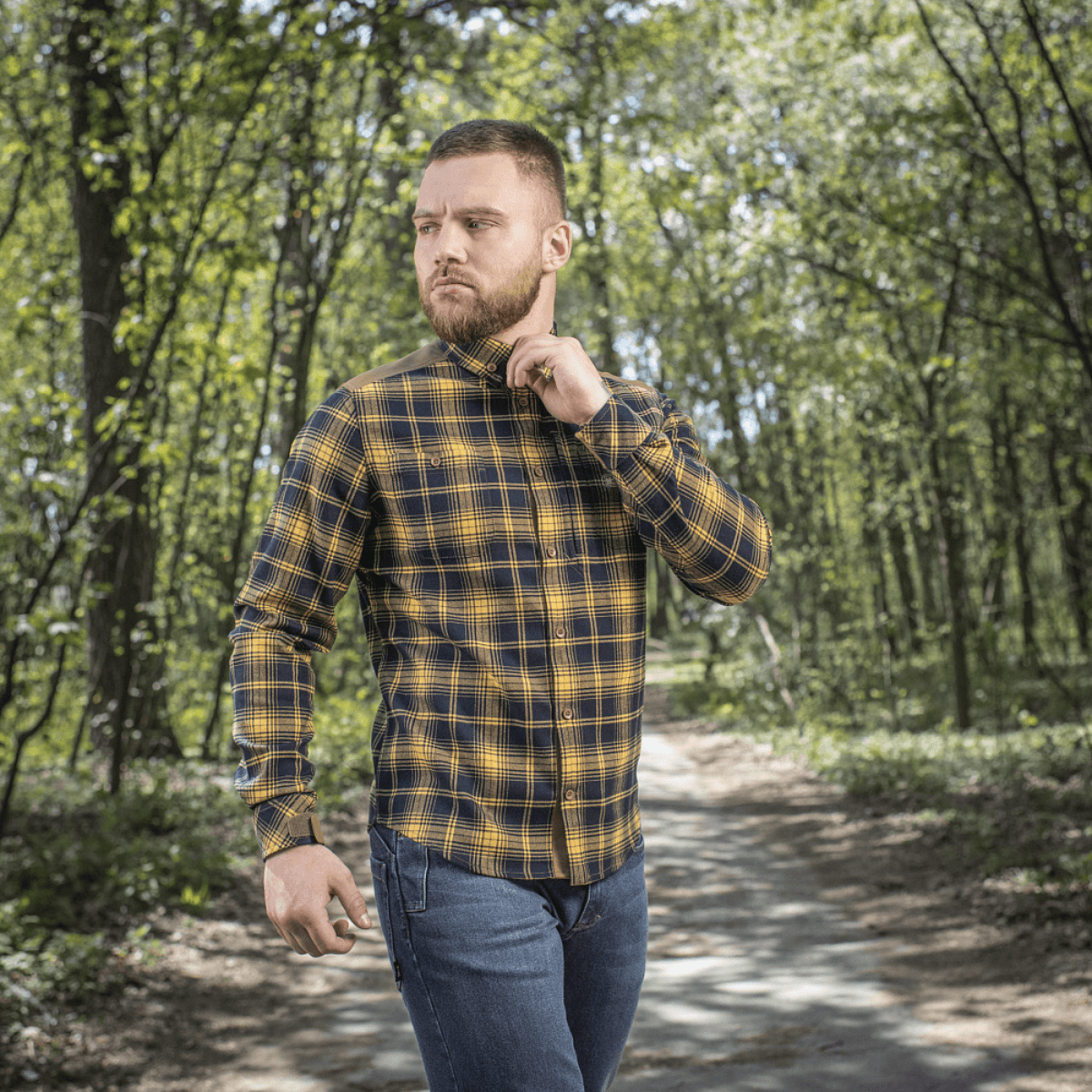 Mand iført M-Tac Redneck Skjorte i Navy Blue/Yellow til arbejde og fritid, justerbare ærmer, går i skovområde.