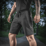 Mand iført M-Tac Shorts Casual Fit Cotton i en park, viser stilrent design og komfortabel pasform, perfekt til sommeraktiviteter.