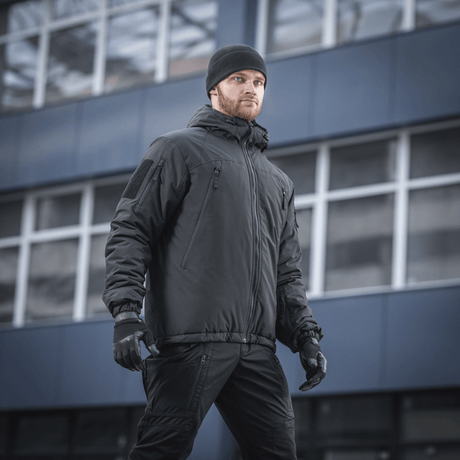 Mand iført M-Tac Alpha Gen.III Pro Vinterjakke med justerbar hætte, perfekt til koldt vejr og hverdagsbrug, baggrund med moderne bygning.