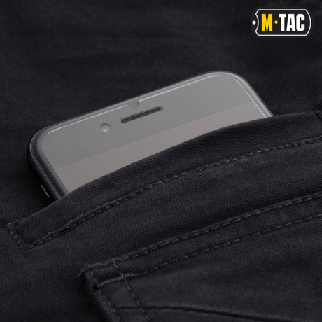 M-Tac Bukser Aggressor Vintage med en telefon i sidelommen, fremhæver buksernes praktiske opbevaringsmuligheder og komfort.