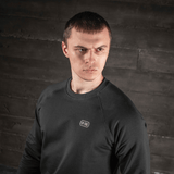 Mand iført M-Tac Raglan Athlete sweatshirt med sort farve og raglanærmer, optimal til sport og hverdag, mod en industriel baggrund.