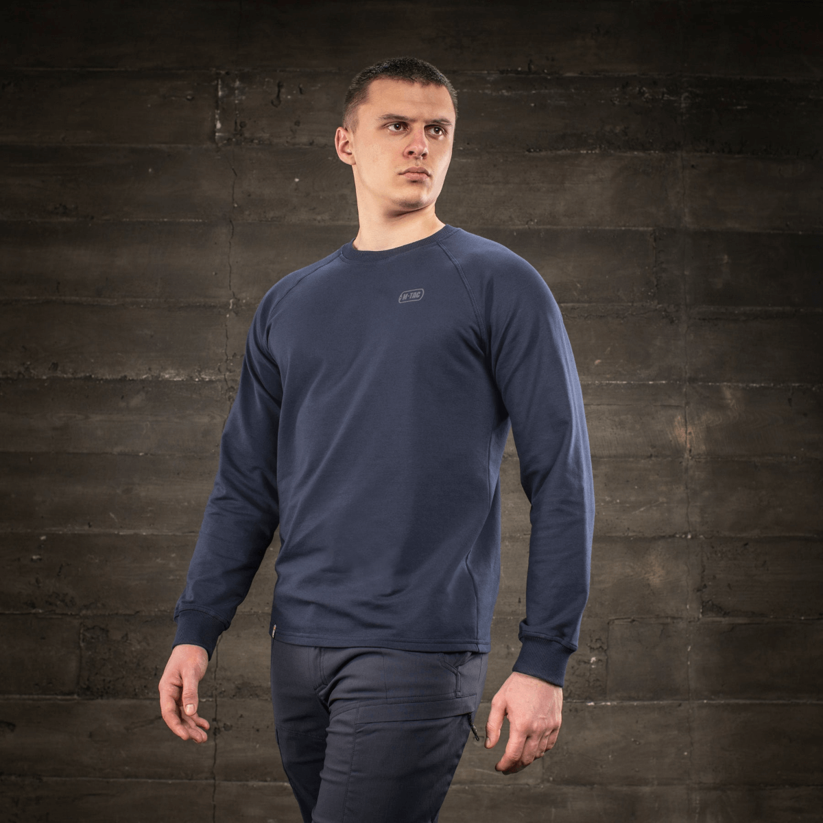 M-Tac Raglan Athlete sweatshirt i minimalistisk design med raglanærmer, set på model mod en rustik baggrund.