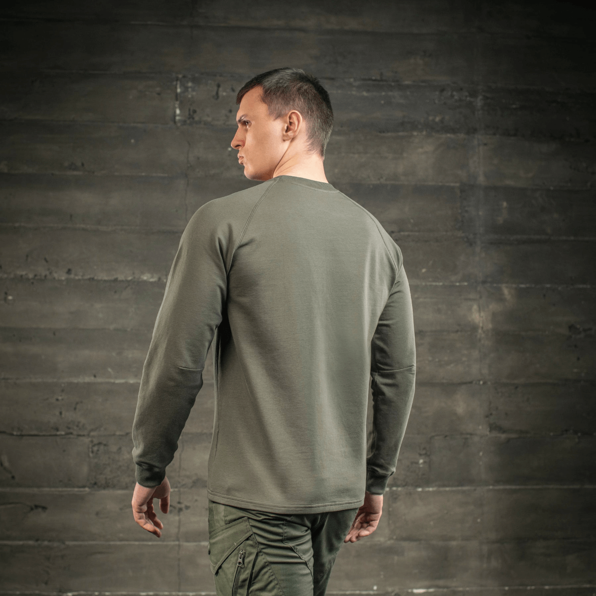 Mand iført M-Tac Raglan Athlete sweatshirt i olivengrøn, set bagfra med raglanærmer til fri bevægelse, perfekt til sport og hverdag.