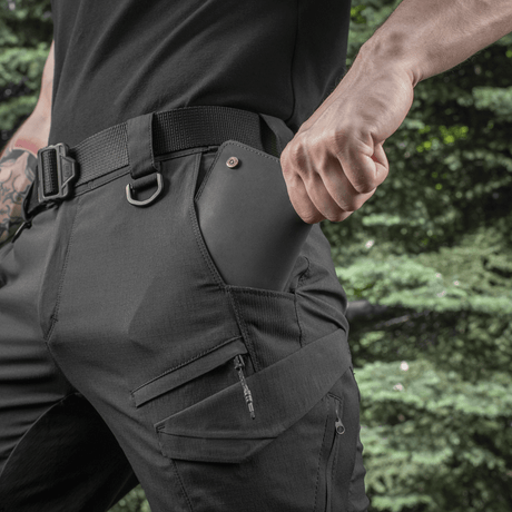 Mand iført M-Tac Aggressor Summer Flex Shorts med D-ringe, funktionelle lommer, perfekt til taktisk brug og udstyr, udendørs baggrund.