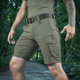 M-Tac Aggressor Summer Flex Shorts i skoven, lette taktiske shorts med Flex Rip-Stop stof, perfekt til udendørsaktiviteter.