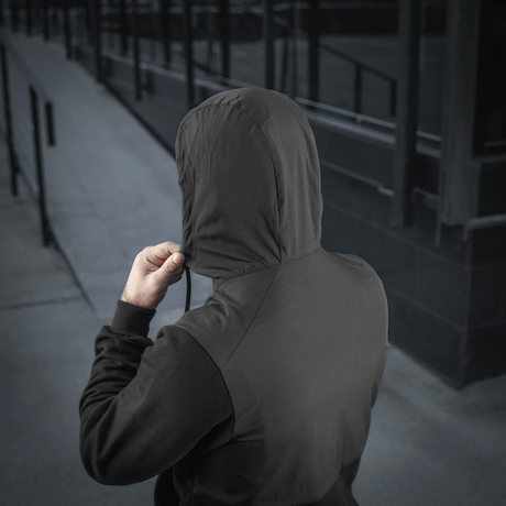 Person wearing M-Tac Pilgrim Bomberjakke with hood up, showing back detail and urban setting.