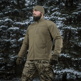 Mand iført M-Tac Combat Fleece Polartec Jakke i snedækket skovmiljø, ideel til taktisk og casual brug.
