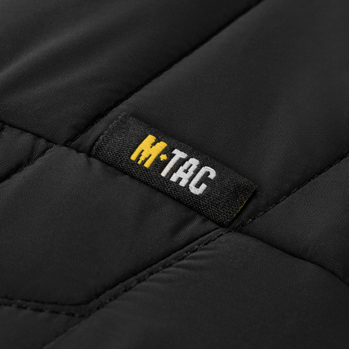 Sort stofdetalje med M-TAC logo på M-Tac Damevest Primaloft, en funktionel og stilfuld kvindevest i vandafvisende nylon.