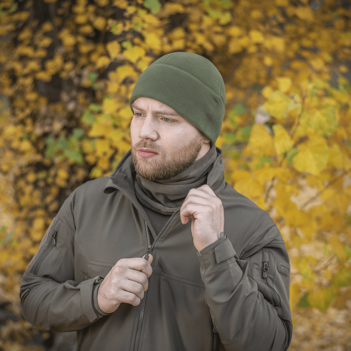Mand iført grøn M-Tac Fleece Polartec Watch Cap i efterårslandskab, ideal til udendørs aktiviteter i kølige og kolde vejrforhold.