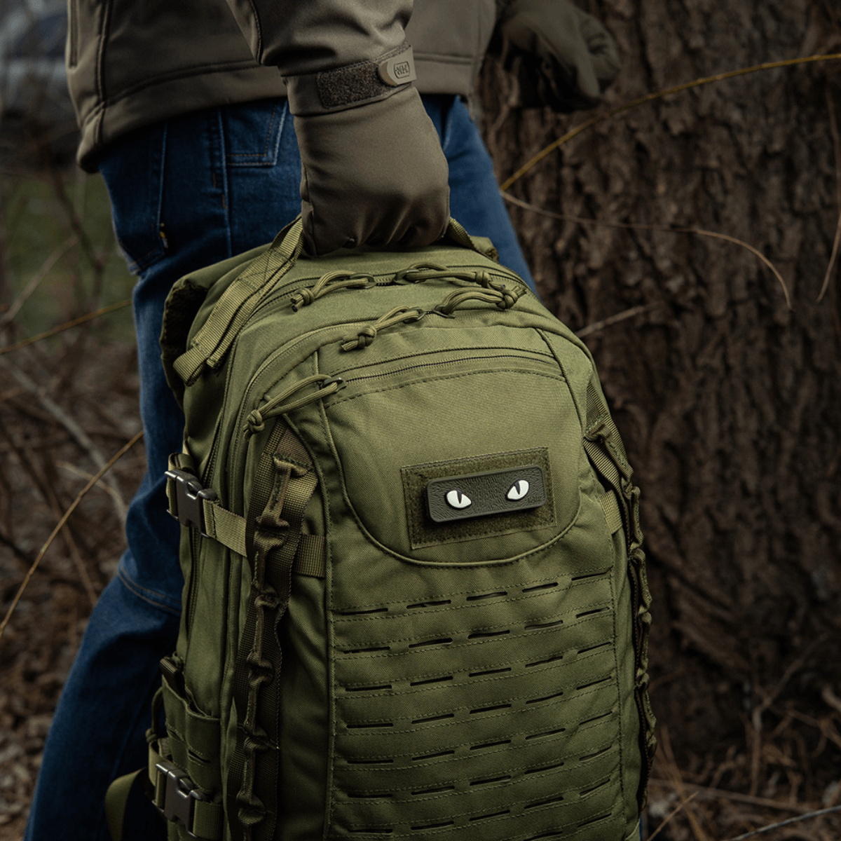 M-Tac Cat Eyes 3D PVC Patch på rygsæk i skov, ideel til taktiske og udendørs aktiviteter, reflekterende design, nem fastgørelse med Velcro.