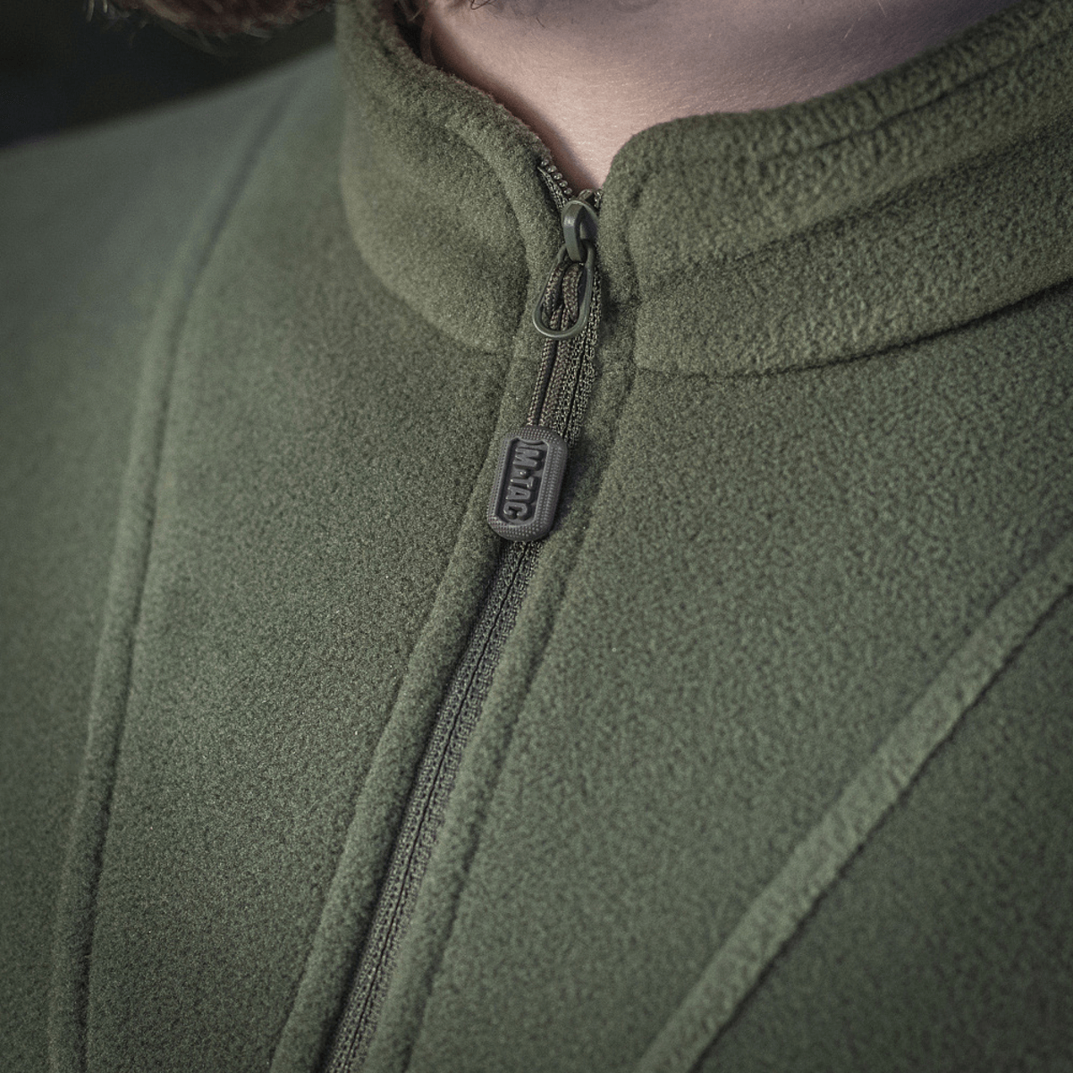 Nærbillede af M-Tac Delta Polartec Fleecejakke i grøn farve, der viser detail af lynlås og stofstruktur, fremstillet af Polartec® Micro Series-fleece.