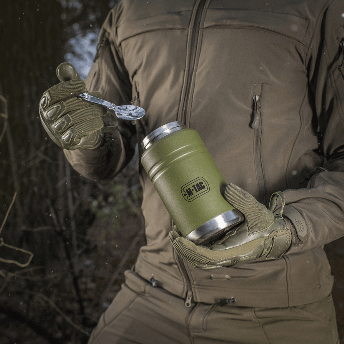 M-Tac Termoflaske 750 ml med Folde-ske bruges udendørs, vist med moderne design og praktisk foldeske, perfekt til camping og vandreture.