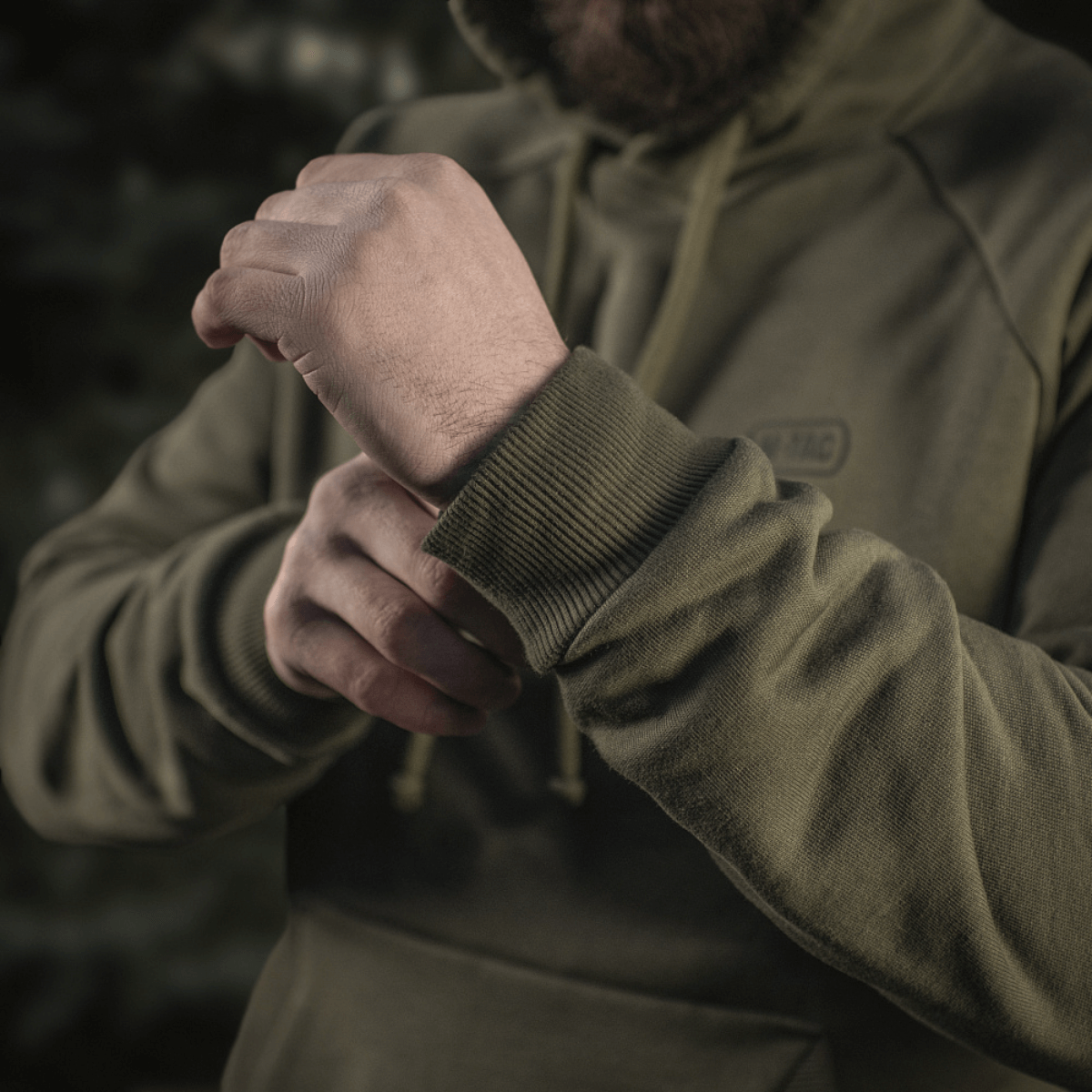 Person iført M-Tac Cotton Raglan Hard Hoodie i 100% bomuld med fleecefor i grøn, viser elastisk manchet på ærmet, perfekt til de køligere årstider.