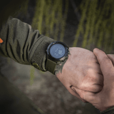 Person wearing M‑Tac Multifunktionelt Taktisk Ur displaying digital time, ideal for outdoor and military use.