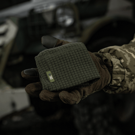 M-Tac Rip-Stop Fleece Hjelmliner vises i en hånd iført taktik handsker i et udendørs militært miljø, kompakt og klar til brug.