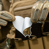 Person iført taktik handsker holder M-Tac Sticker Valkyrie foran en taske.