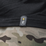 Nærbillede af M-Tac T-Shirt Surf Club tag, sort stof med kamuflagerprint i baggrunden