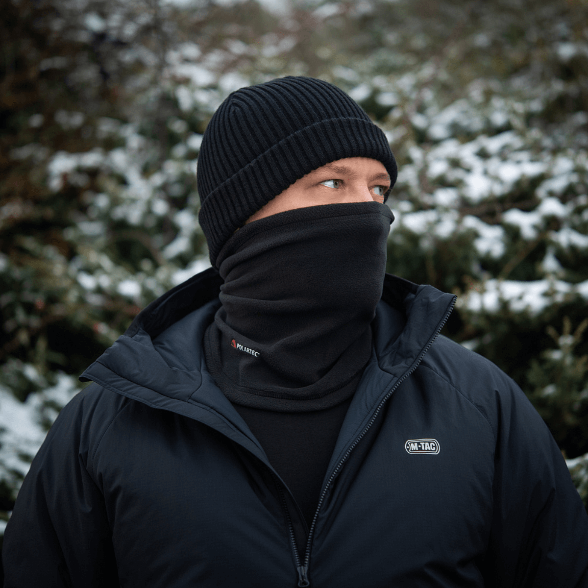 Mand iført M-Tac Tube Scarf Polartec i sneklædt landskab, beskyttet mod kulde med multifunktionel halstørklæde og jakke.