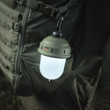 M-Tac Turist Hængelampe hængende på rygsæk, ideel til camping og jagt. LED-lys med tre funktioner, opladning via USB, robust og funktionel.
