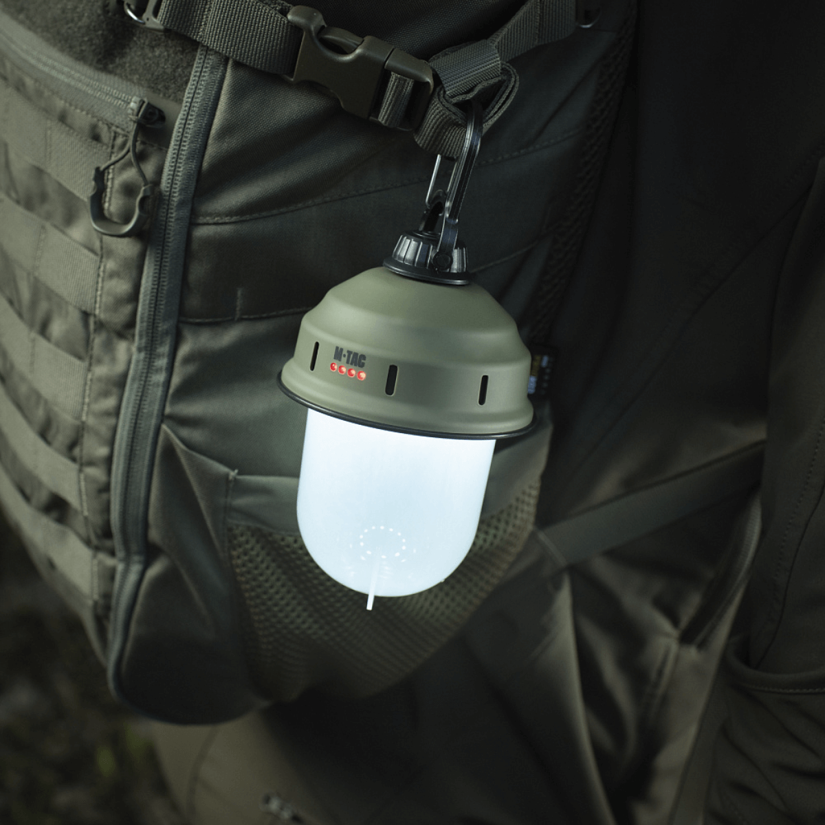 M-Tac Turist Hængelampe hængende på rygsæk, ideel til camping og jagt. LED-lys med tre funktioner, opladning via USB, robust og funktionel.